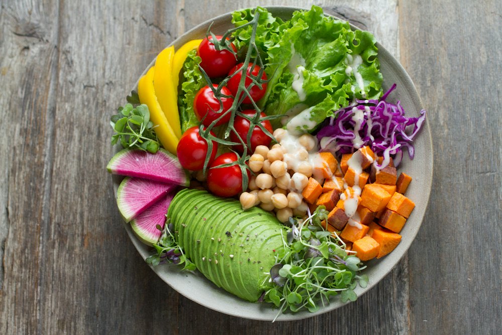 A bowl of chickpeas, roasted sweet potato, avocado, and fresh vegetables